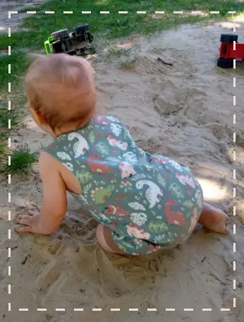 Baby in einem handgemachten Body spielt fröhlich in einer Sandkiste, hervorhebend die spielend-leichte Qualität unserer Kindermode